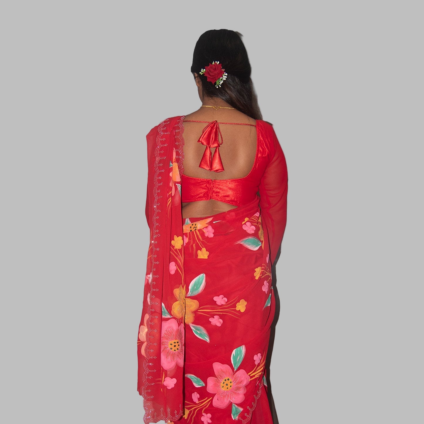 Red saree with floral patterns worn by a person on a gray background