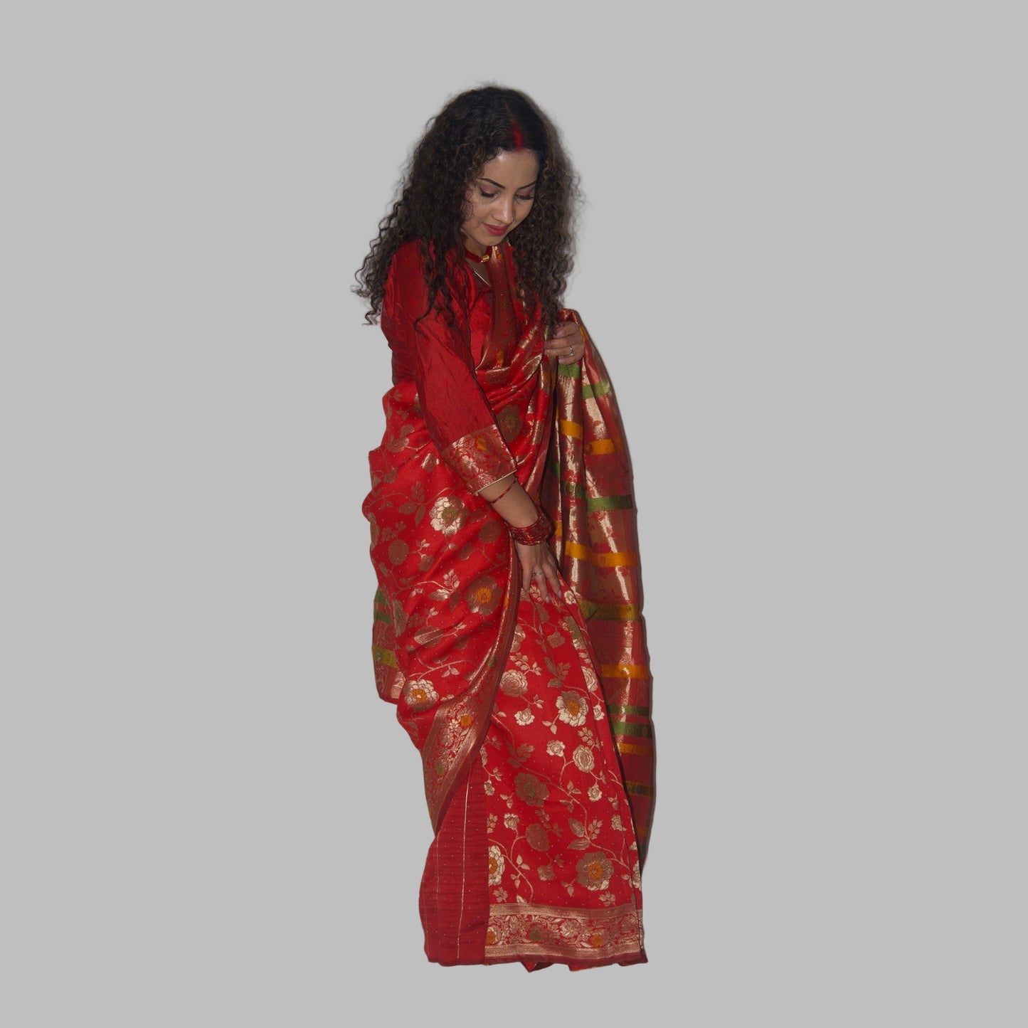 Woman wearing a red saree with gold patterns on a white background