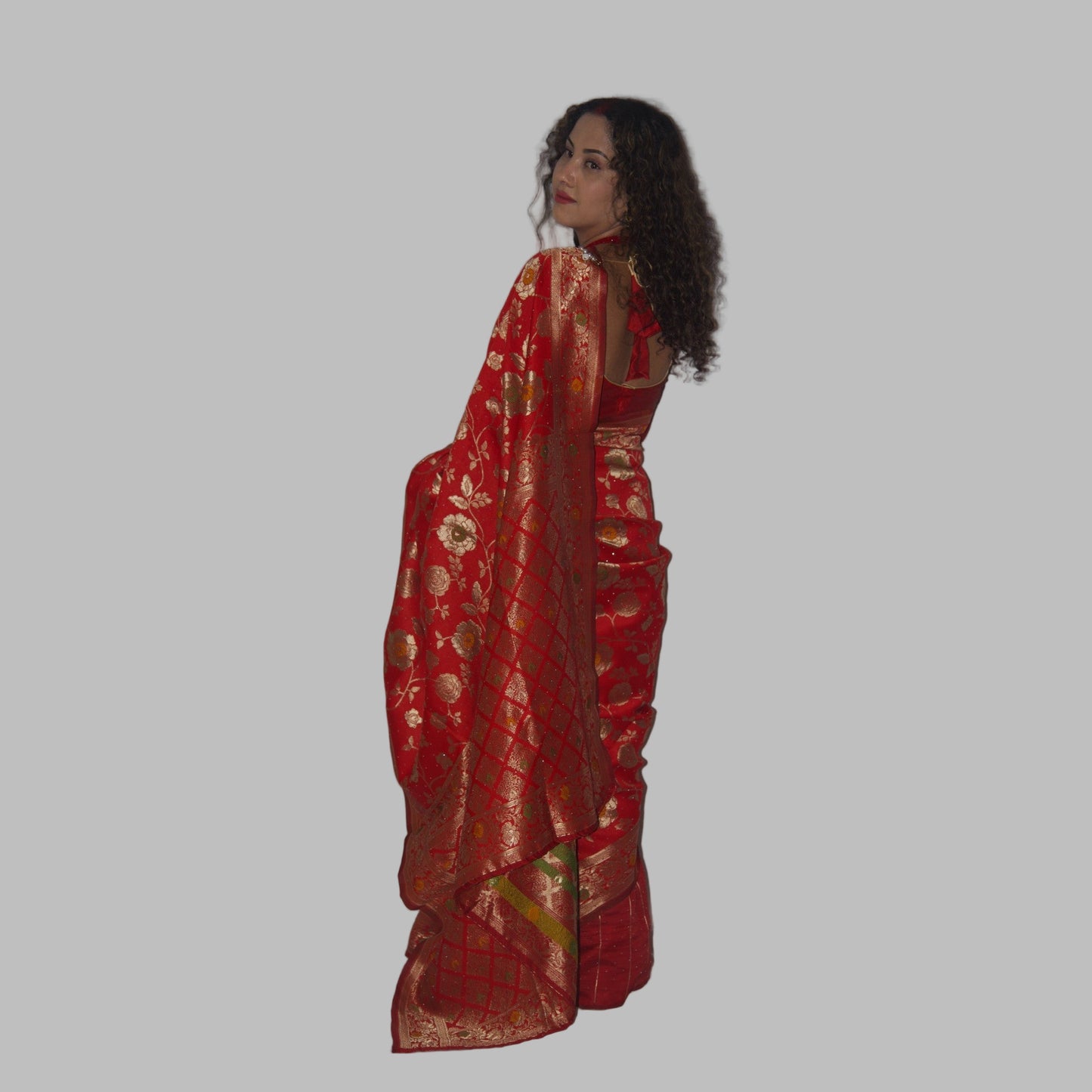 Woman wearing a red saree with gold patterns on a white background