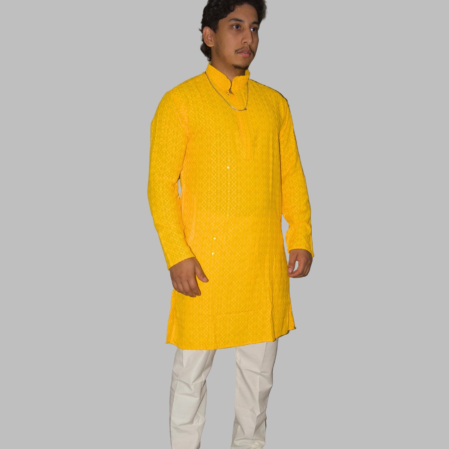 Man wearing a bright yellow kurta with white pants against a plain background