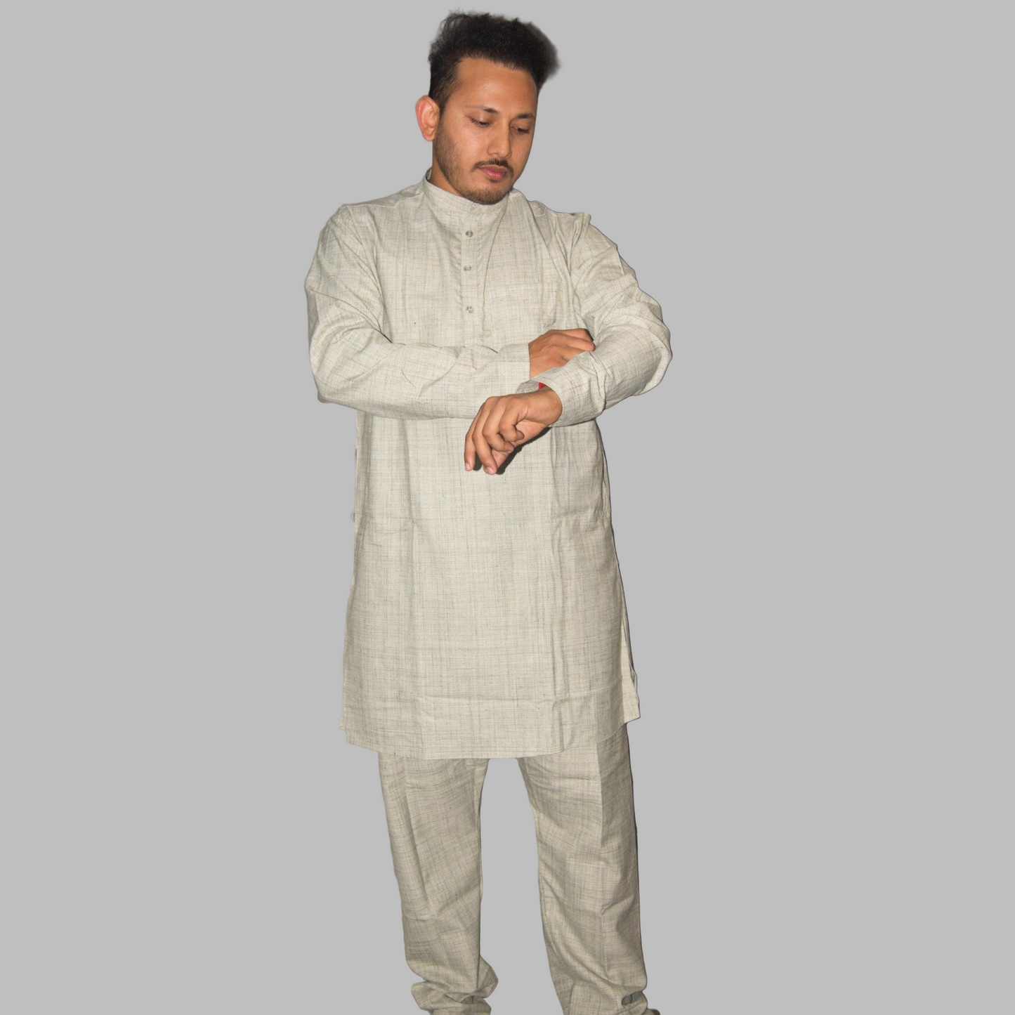 Man wearing a light-colored traditional outfit against a plain wall.