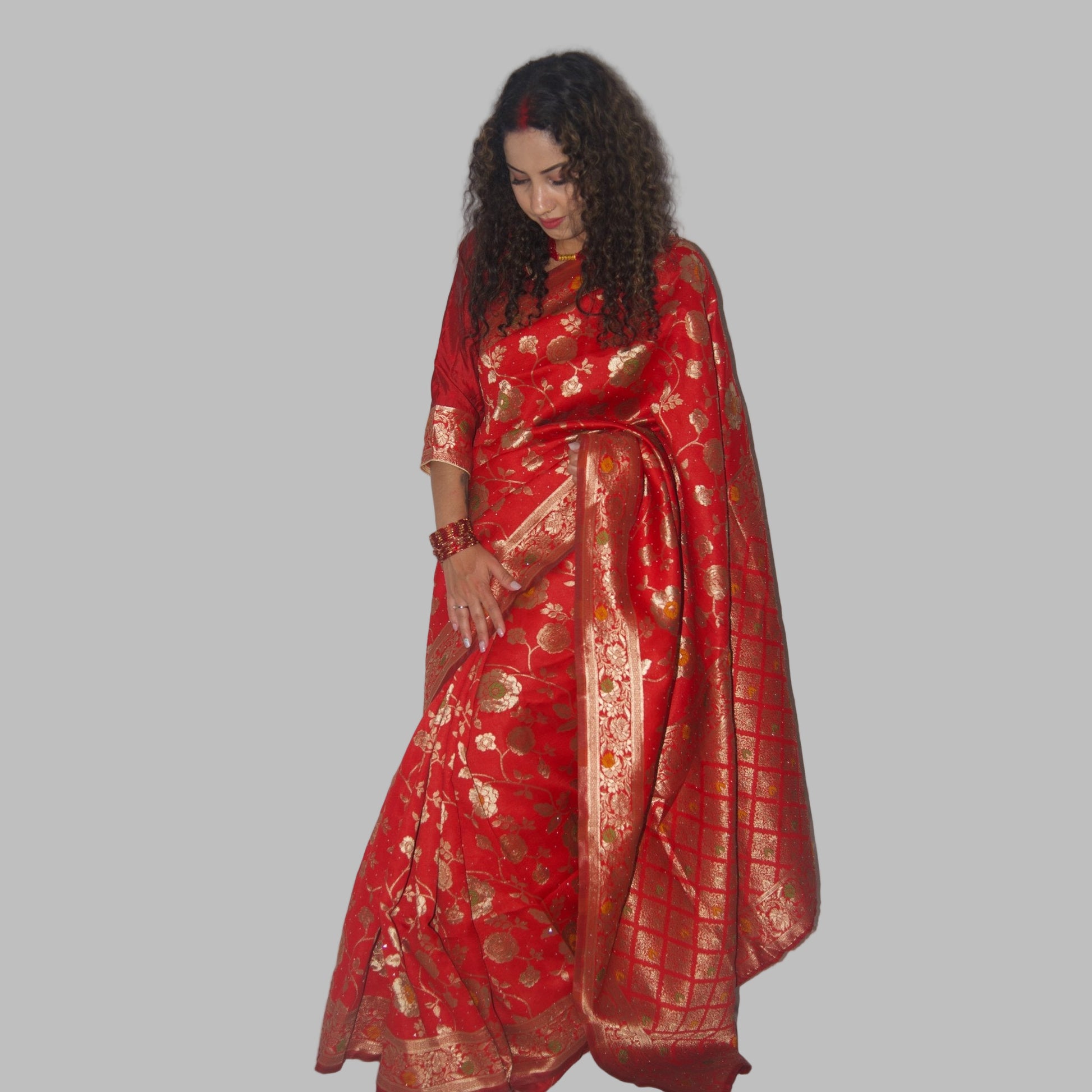 Woman wearing a red saree with gold patterns on a white background