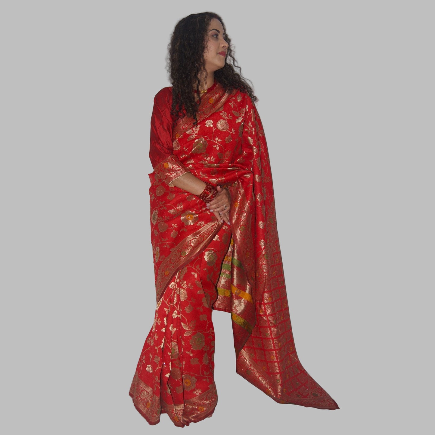 Woman wearing a red saree with gold patterns on a white background