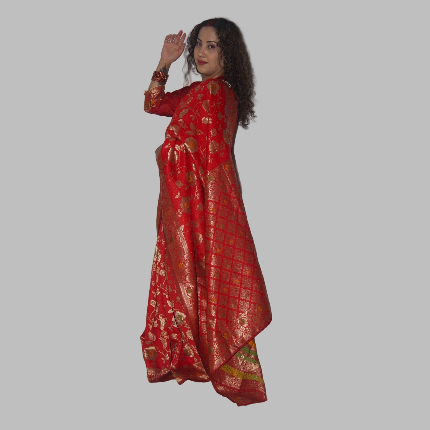 Woman wearing a red saree with gold patterns against a white background