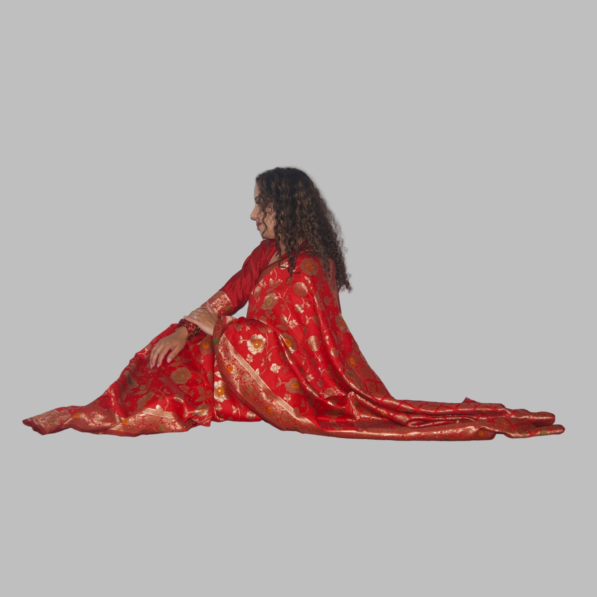 Woman in a red saree sitting on a white curtain