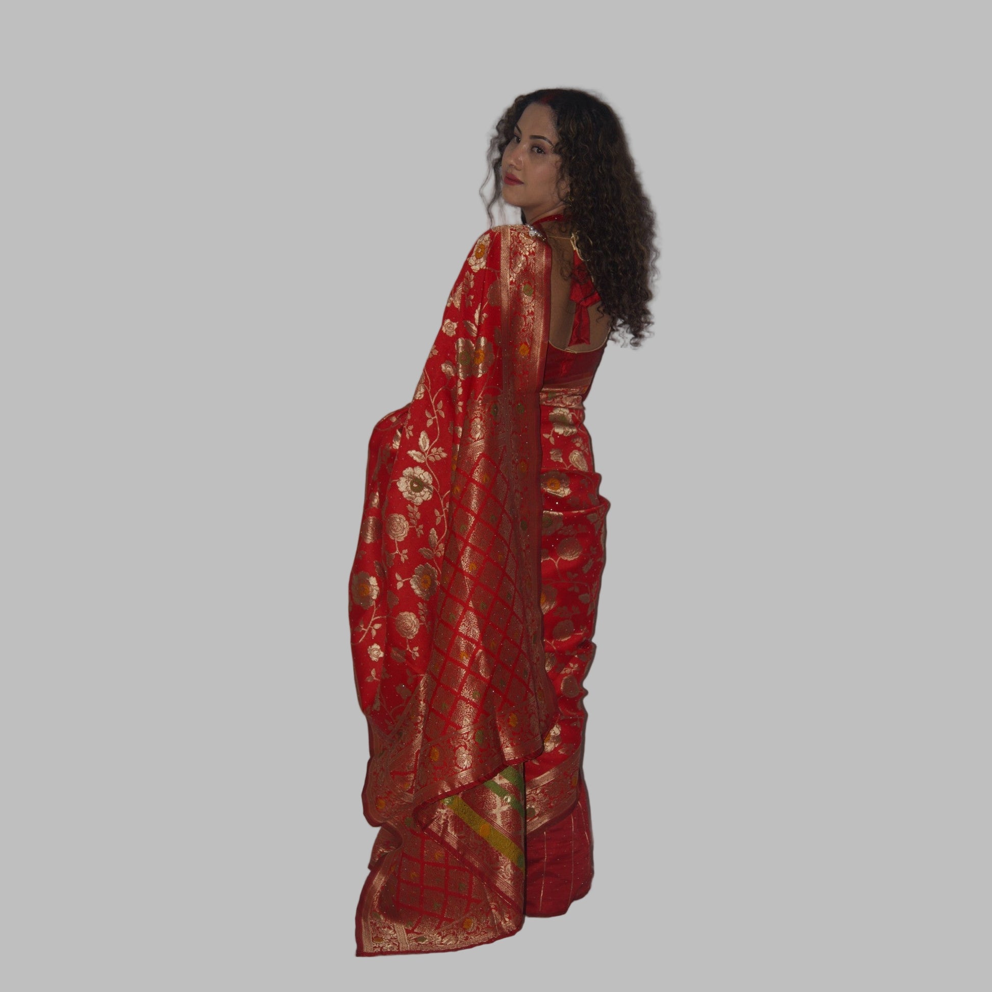 Woman wearing a red saree with gold patterns on a white background