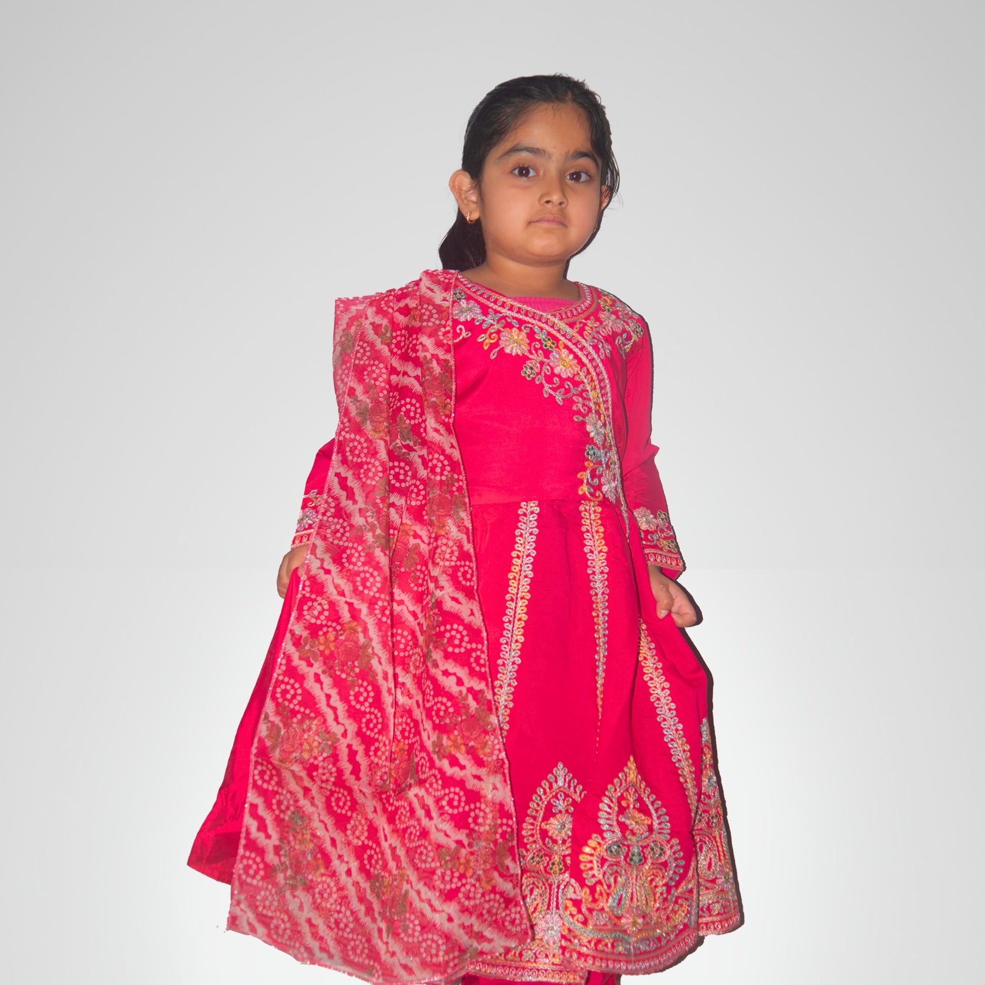 Young girl wearing a pink traditional outfit with intricate patterns on a white background