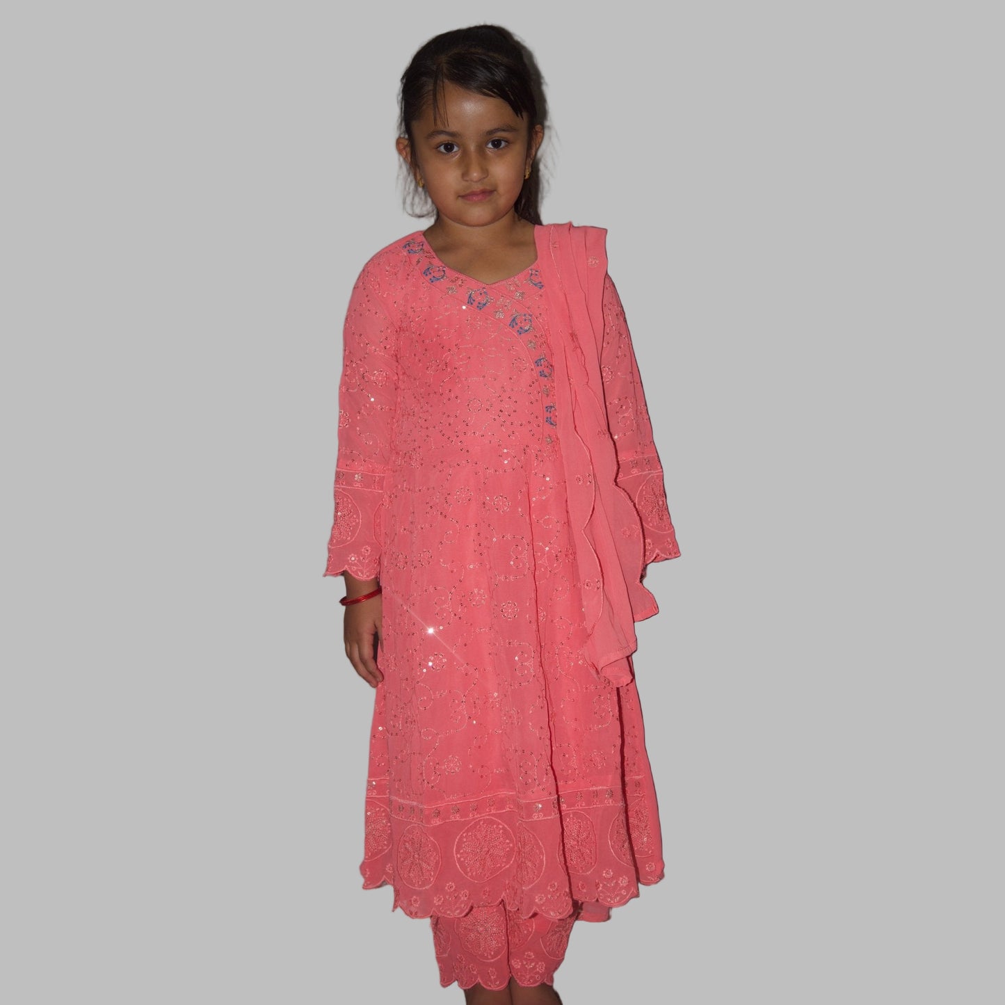 Young girl wearing a pink dress against a plain wall