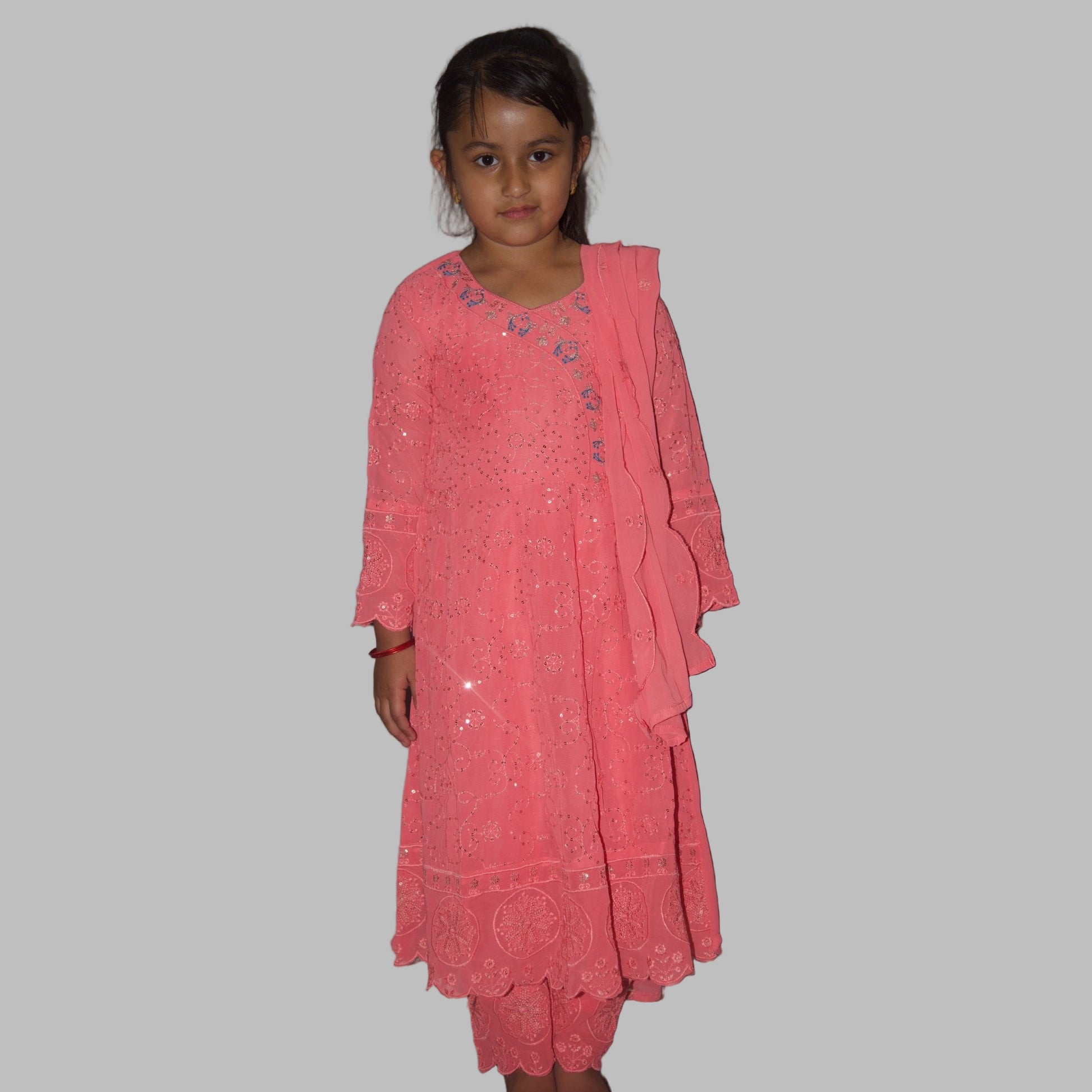 Young girl wearing a pink dress against a plain wall