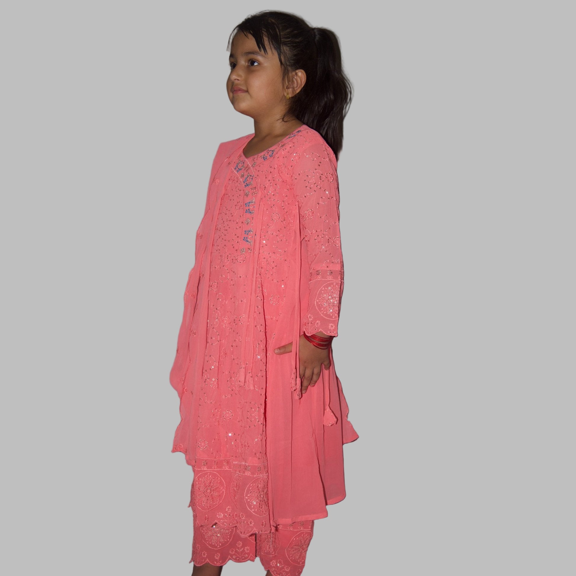 Young girl wearing a pink traditional outfit against a plain wall.