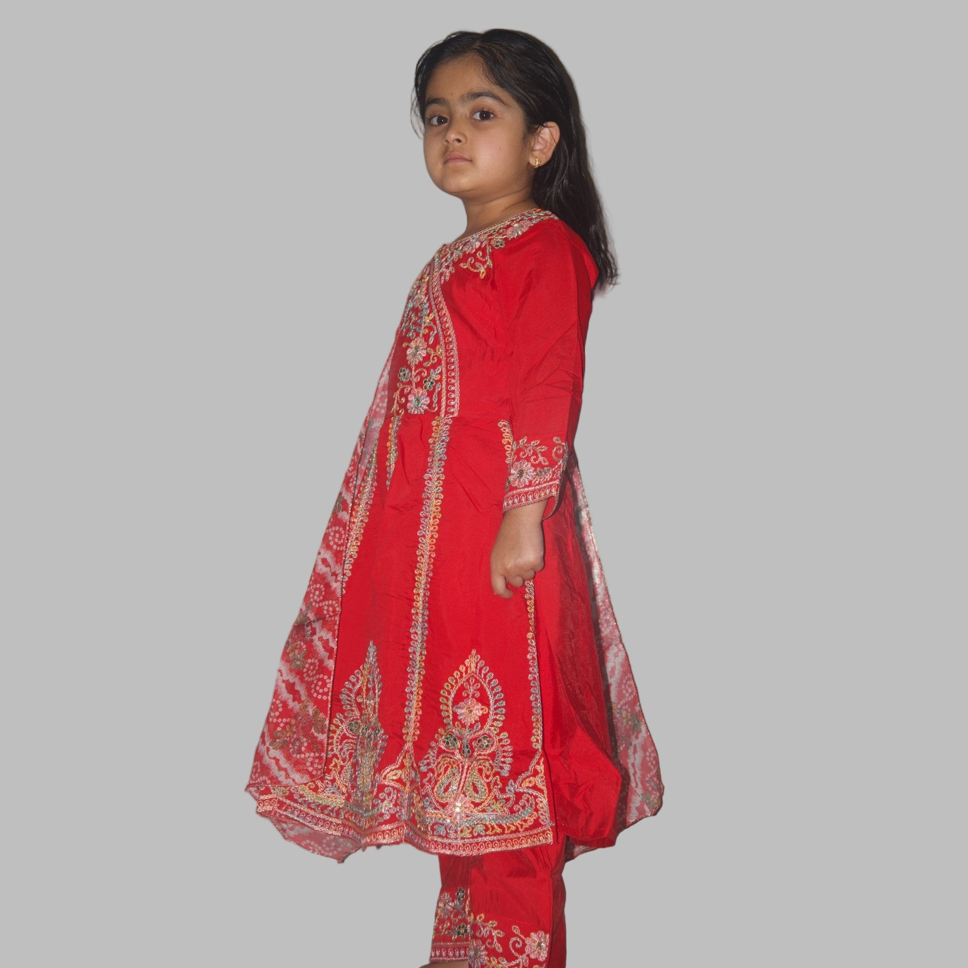 Young girl wearing a red embroidered traditional outfit against a plain background