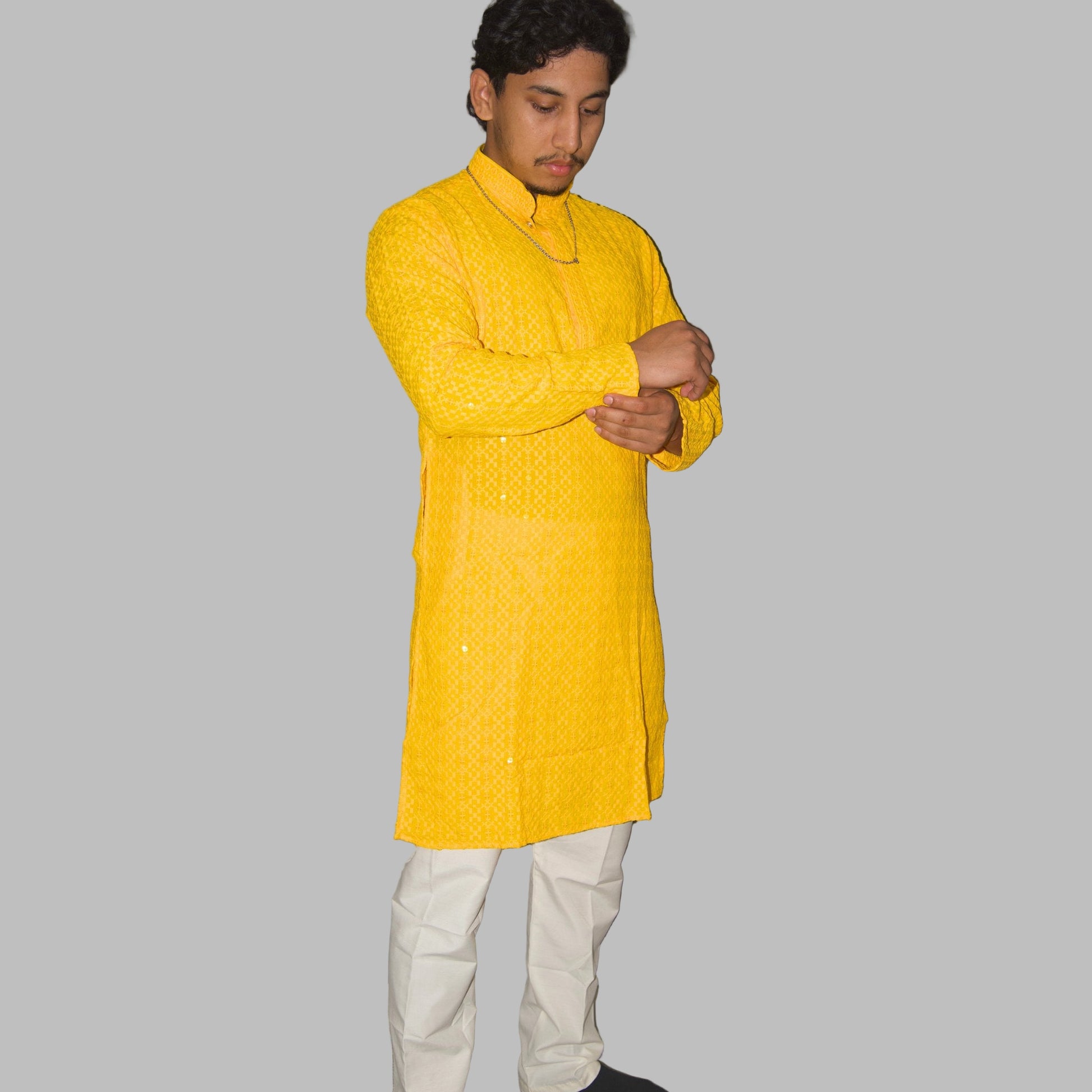 Person wearing a yellow kurta with white pants against a plain background