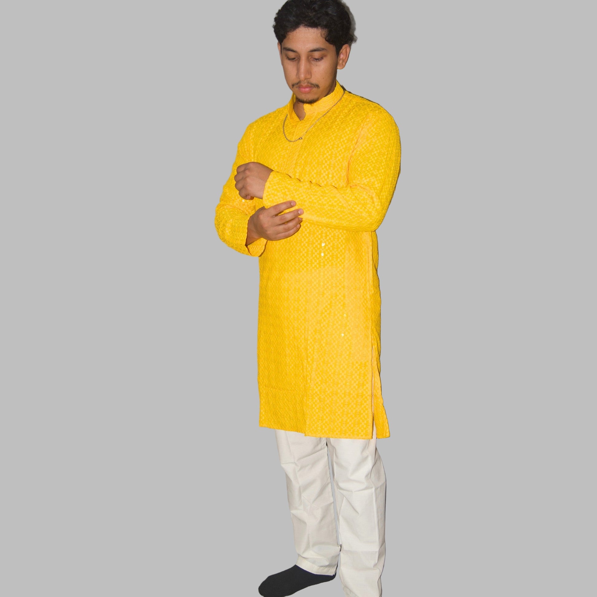Person wearing a bright yellow kurta with white pants against a plain background