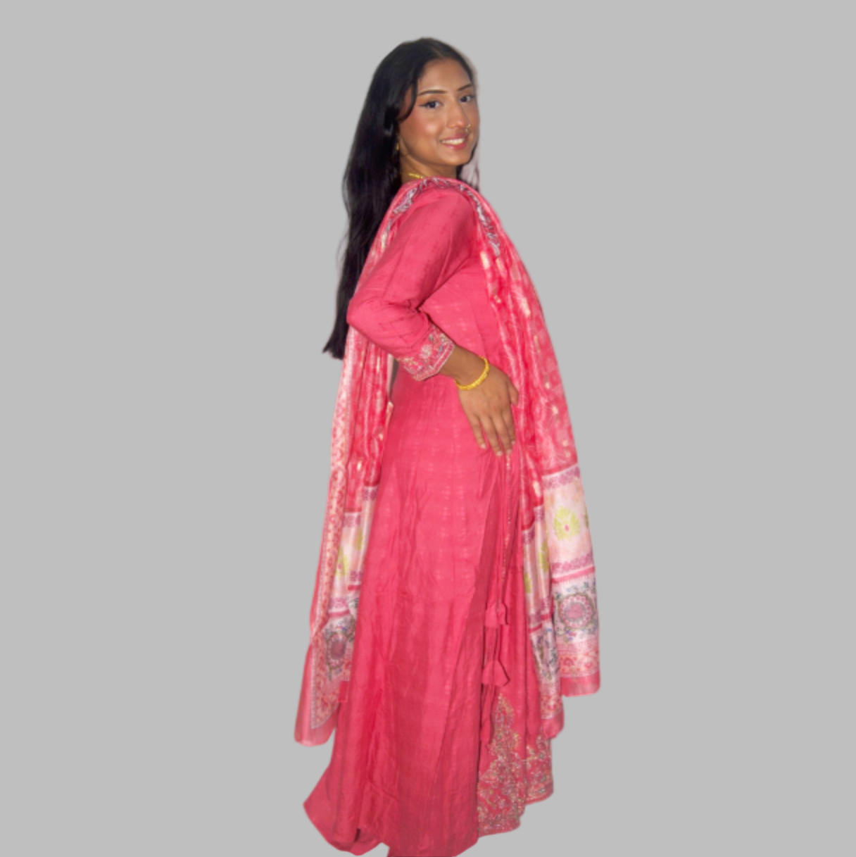 Woman wearing a pink traditional outfit with a matching dupatta on a gray background