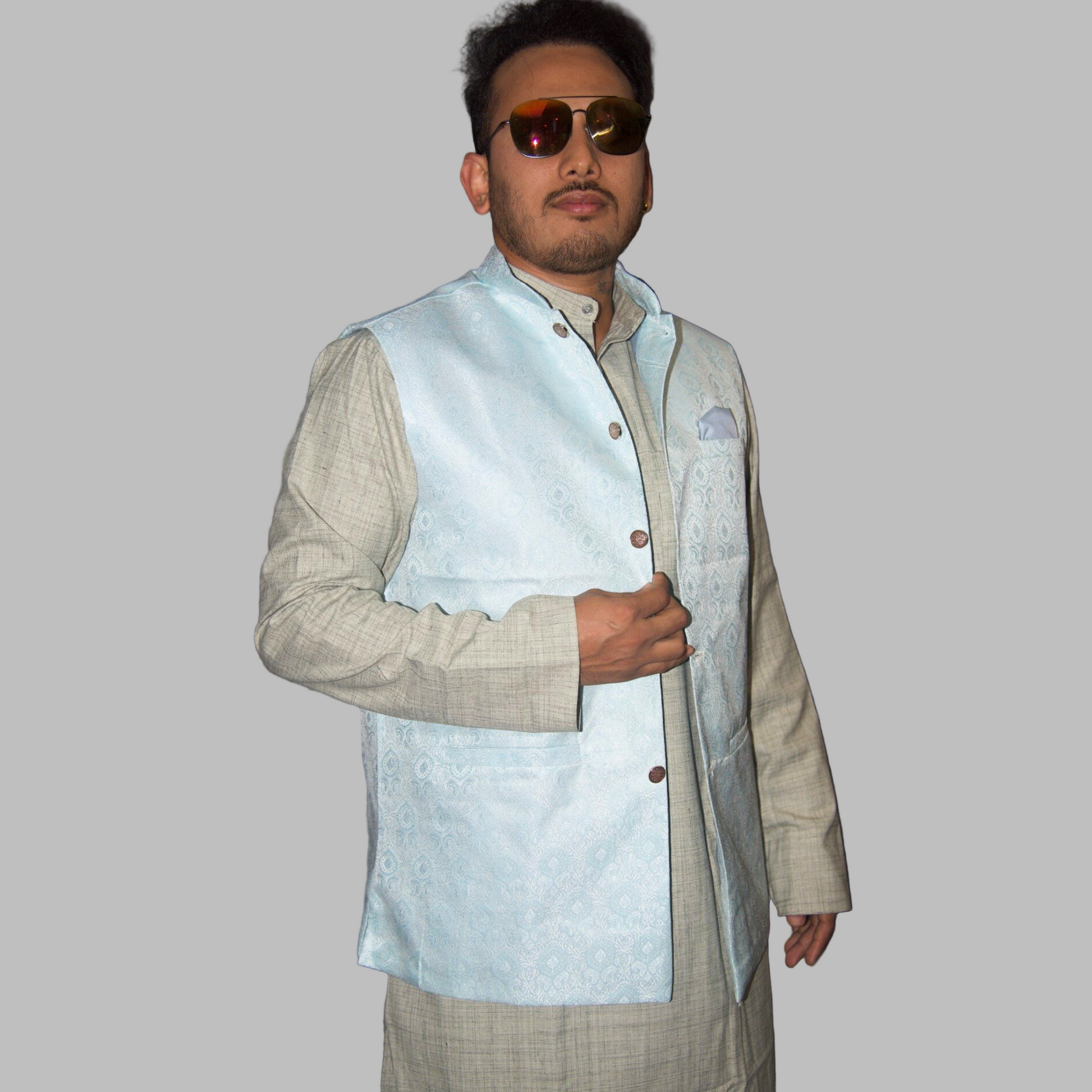 Man wearing a light blue vest over a patterned shirt against a plain background