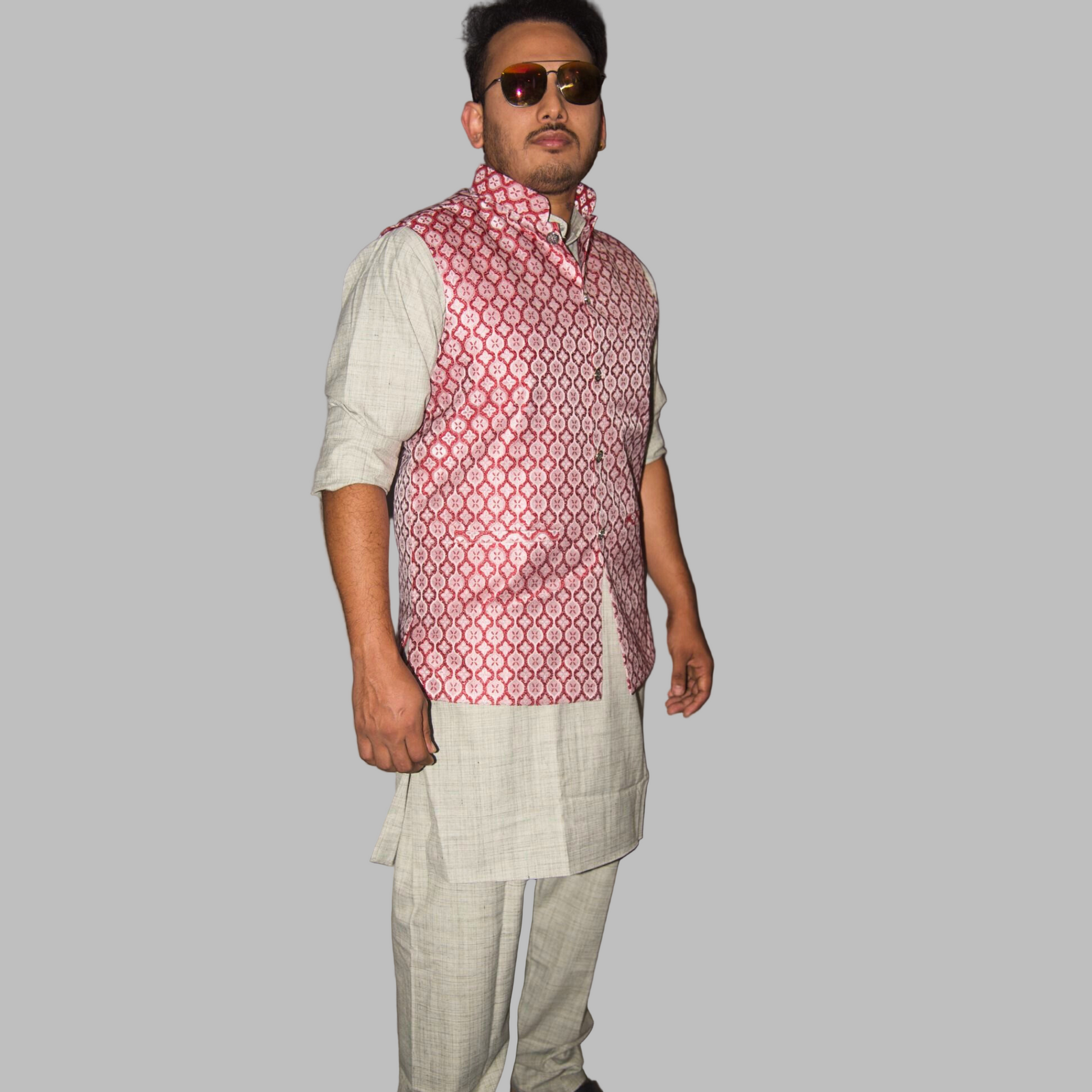Man wearing a patterned vest over a white shirt and light pants against a plain background