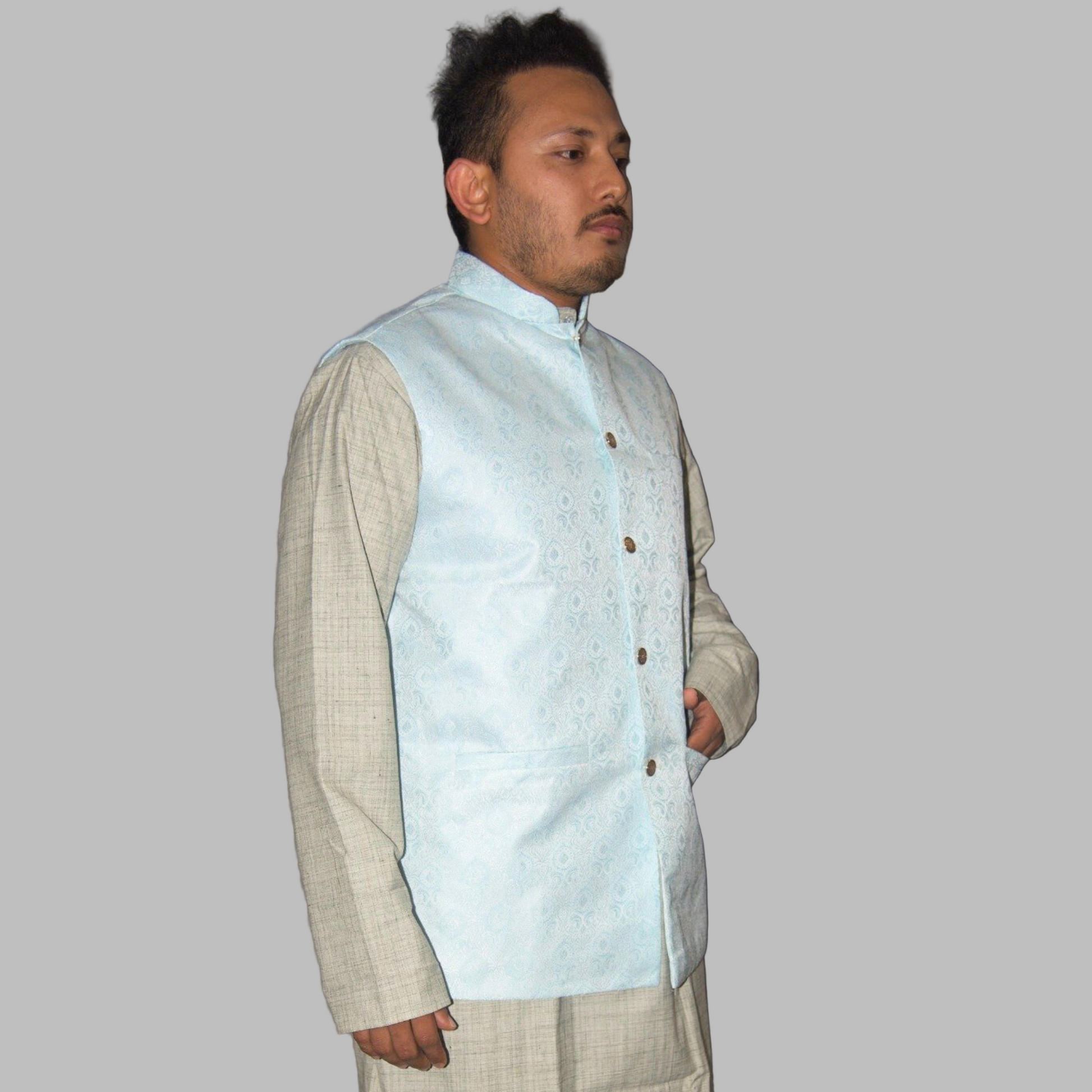 Man wearing a light blue vest over a beige shirt against a plain background