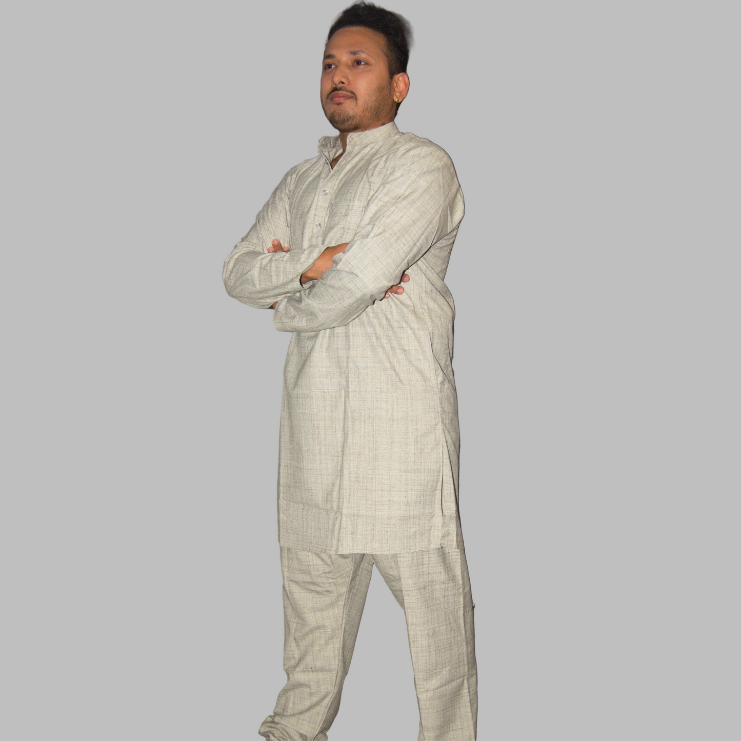 Man wearing a light-colored traditional outfit standing against a plain wall.